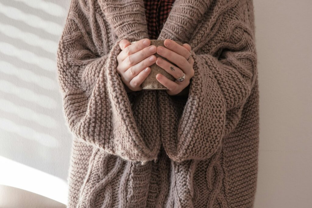 Mains enfouies dans les manches d'un gros pull en maille tenant une tasse chaude