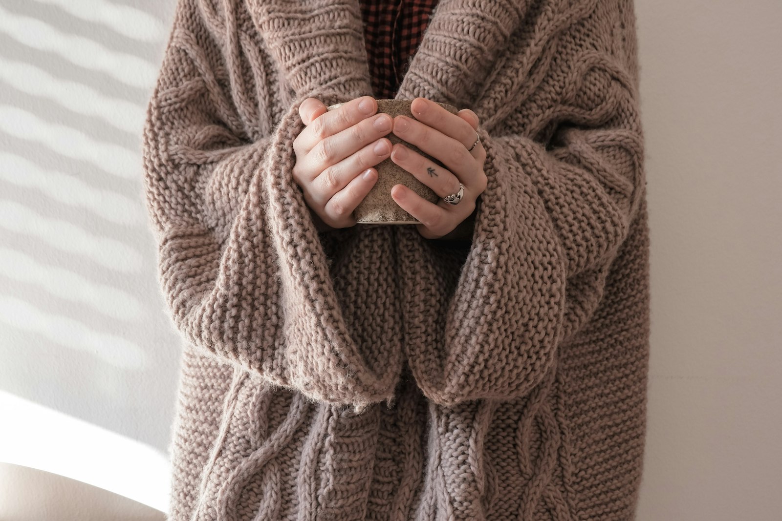 Mains enfouies dans les manches d'un gros pull en maille tenant une tasse chaude