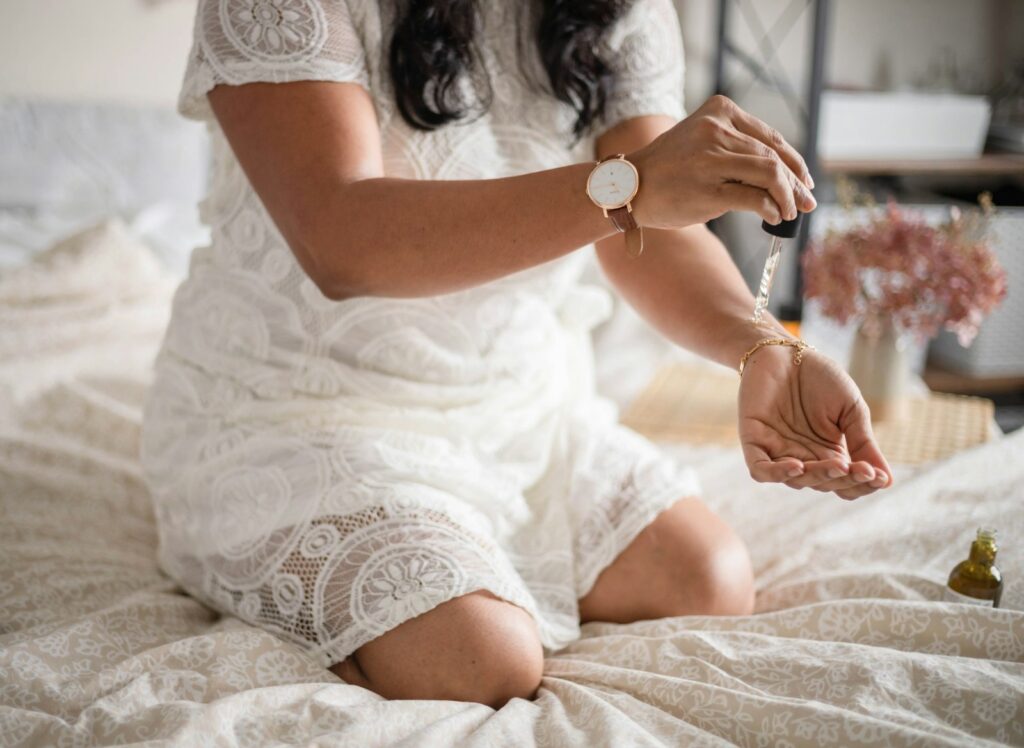 Femme assise sur un lit déposant quelques gouttes de soin sur sa main