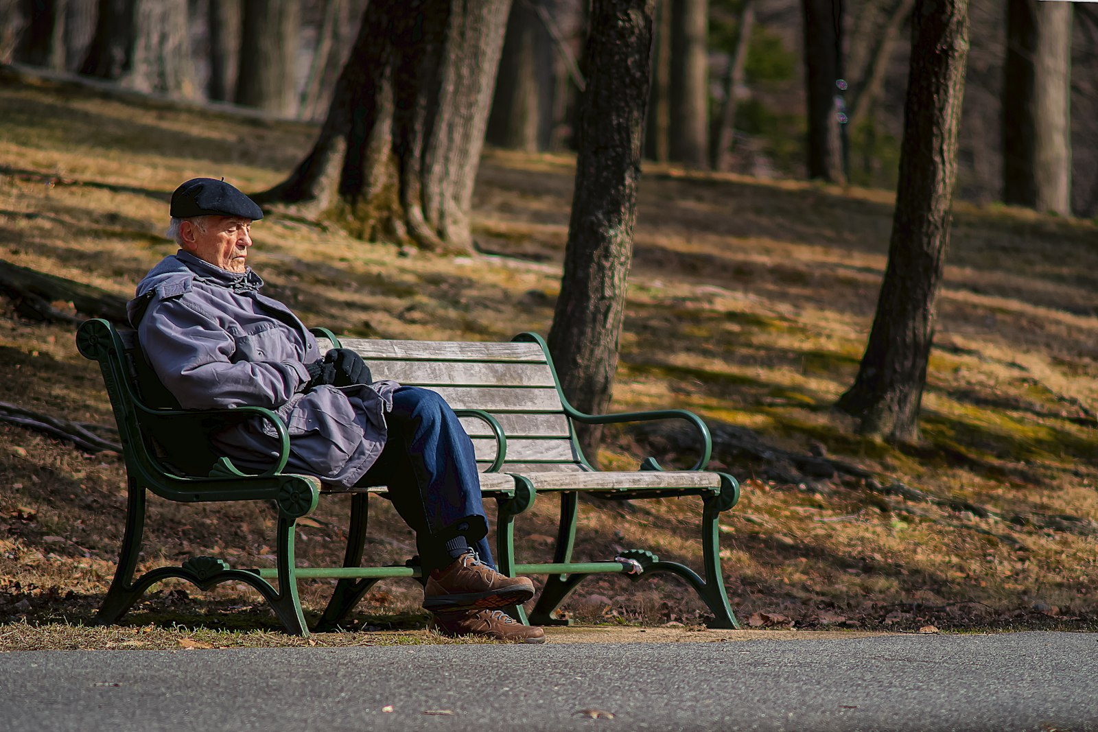 Homme âgé en veste sombre assis sur un banc de parc au soleil
